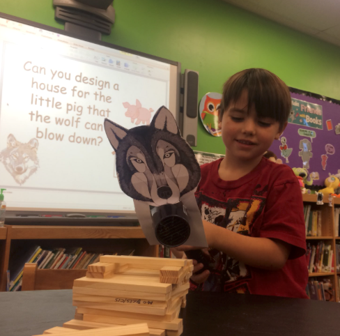 A kindergarten student testing out his KEVA plank house for the Three Little Pigs