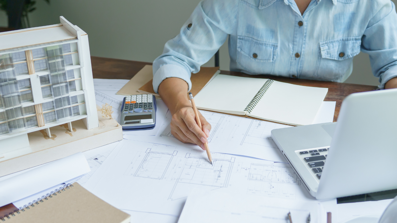 Person writing on architectural blueprints with calculator