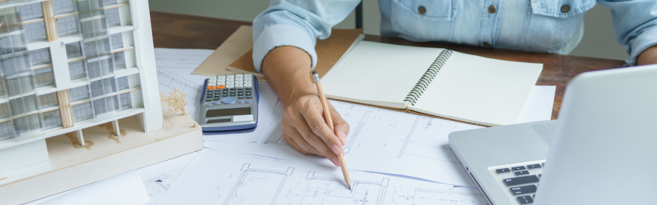 Person writing on architectural blueprints with calculator