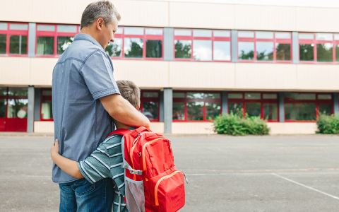 Father hugging son with backpack at school 