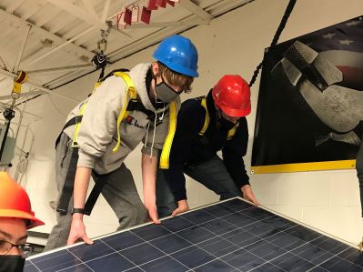Two students on roof installing a solar panel in a CTE classroom.