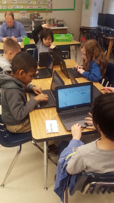 Students learning the alphabet on laptops in class