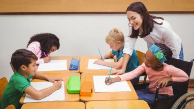 several smiling young students working at a table with a teacher in a classroom